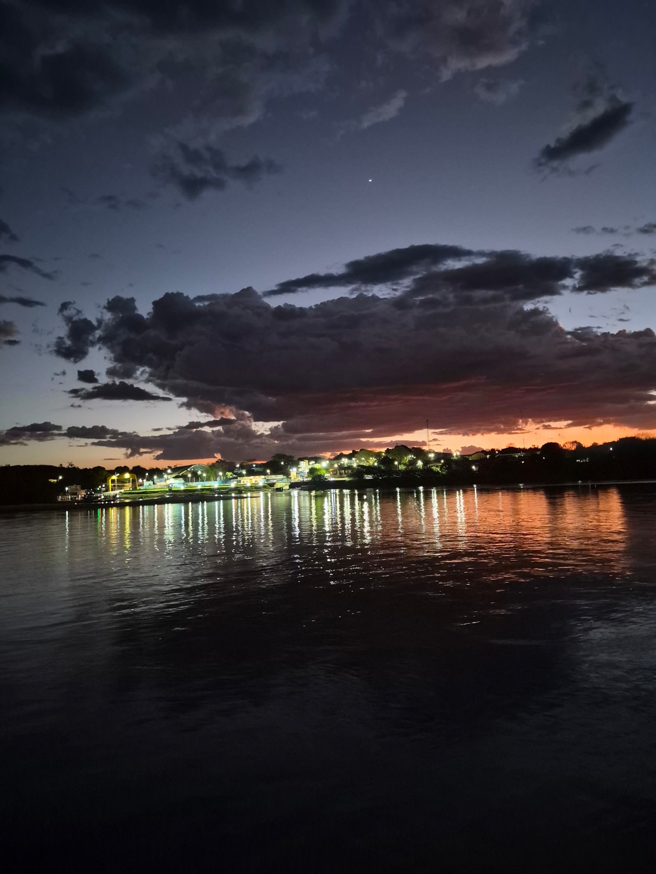 Luzes da cidade refletindo no rio sob um céu de entardecer